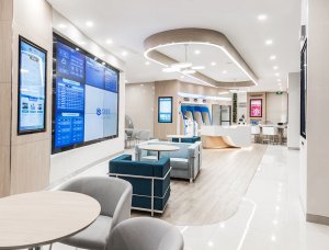 A modern, well-lit lobby with a large screen displaying information, comfortable seating areas, and a reception desk.